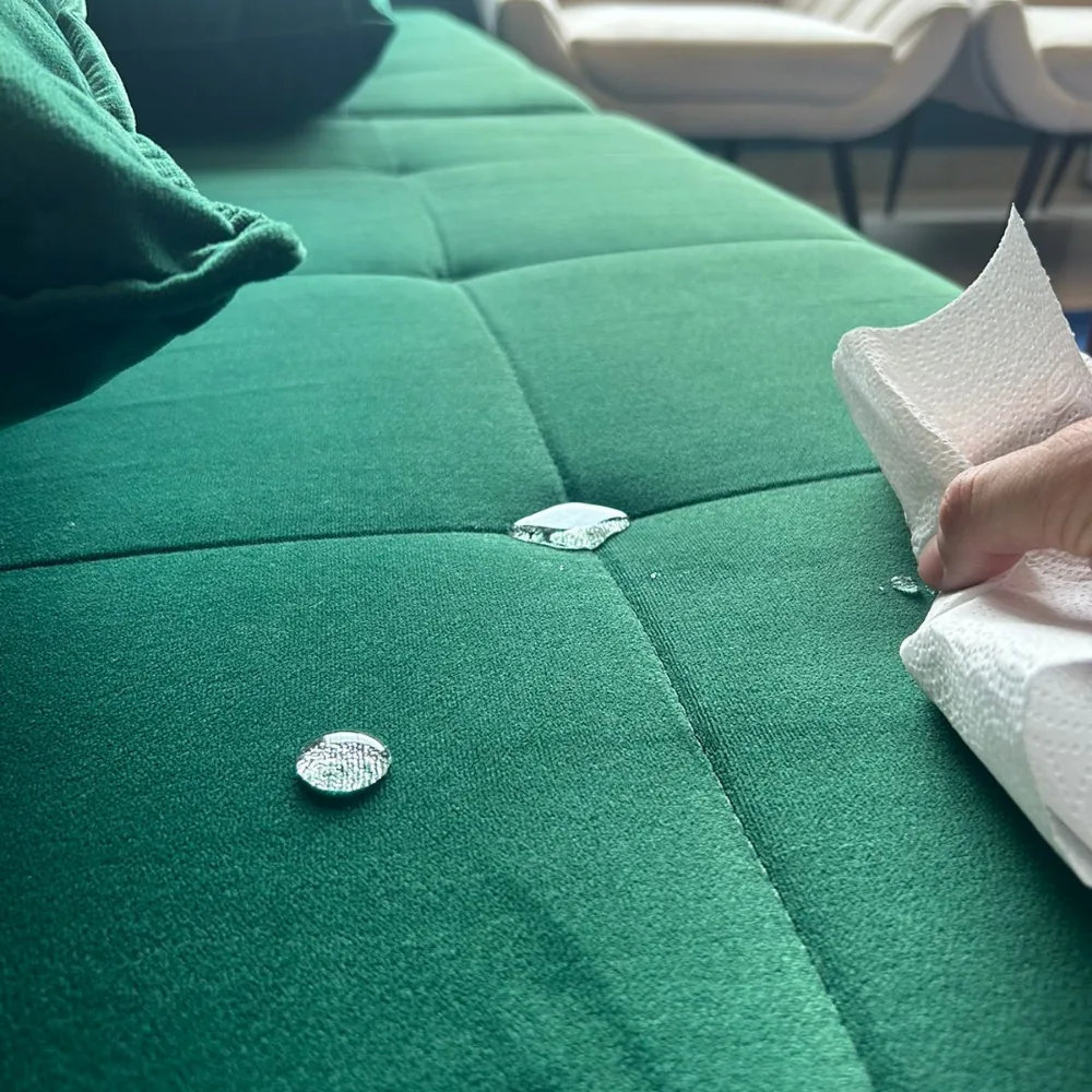 Água repelida sobre sofá impermeabilizado sendo removida com papel toalha